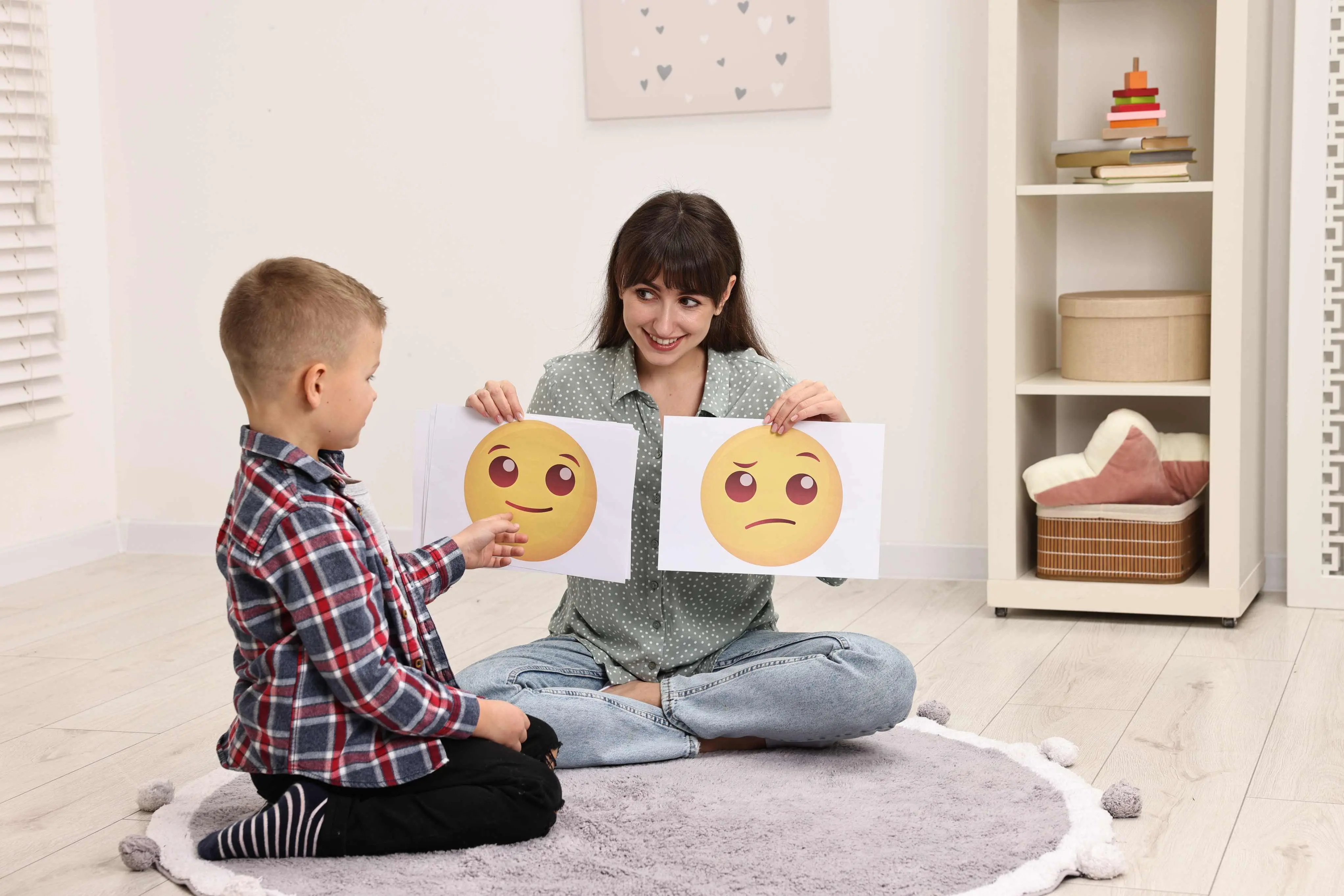 Imagem de uma criança apontando para placas com emojis, para ilustrar matéria sobre comunicação alternativa atrapalha a fala? Entenda benefícios desse método para crianças autistas.