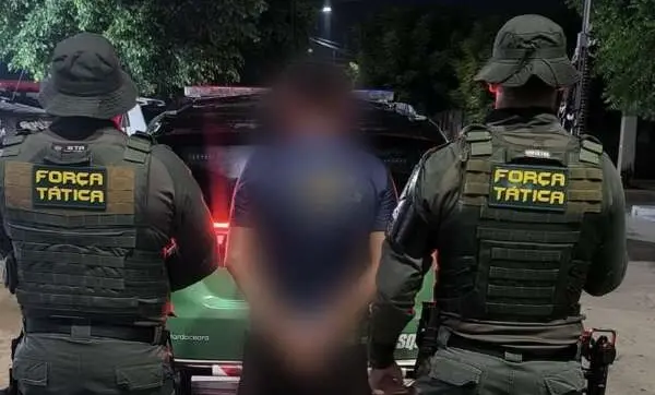 Dois policiais militares de costas e suspeito no meio, entre eles, com imagem borrada.