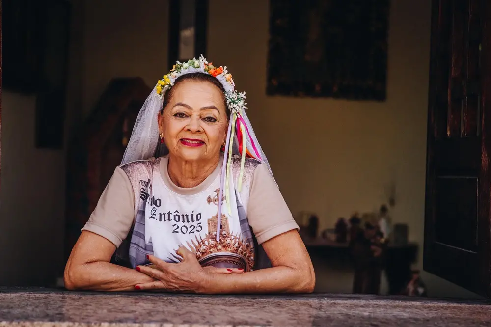 Na imagem, uma mulher madura, de pele clara e cabelos presos, olha para a câmera com um sorriso gentil na imagem 