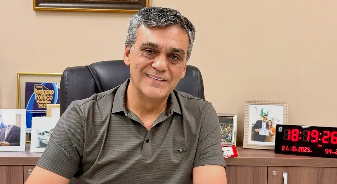 Naumi Amorim sentado no gabinete de prefeito. Ele olha para a câmera e sorri.