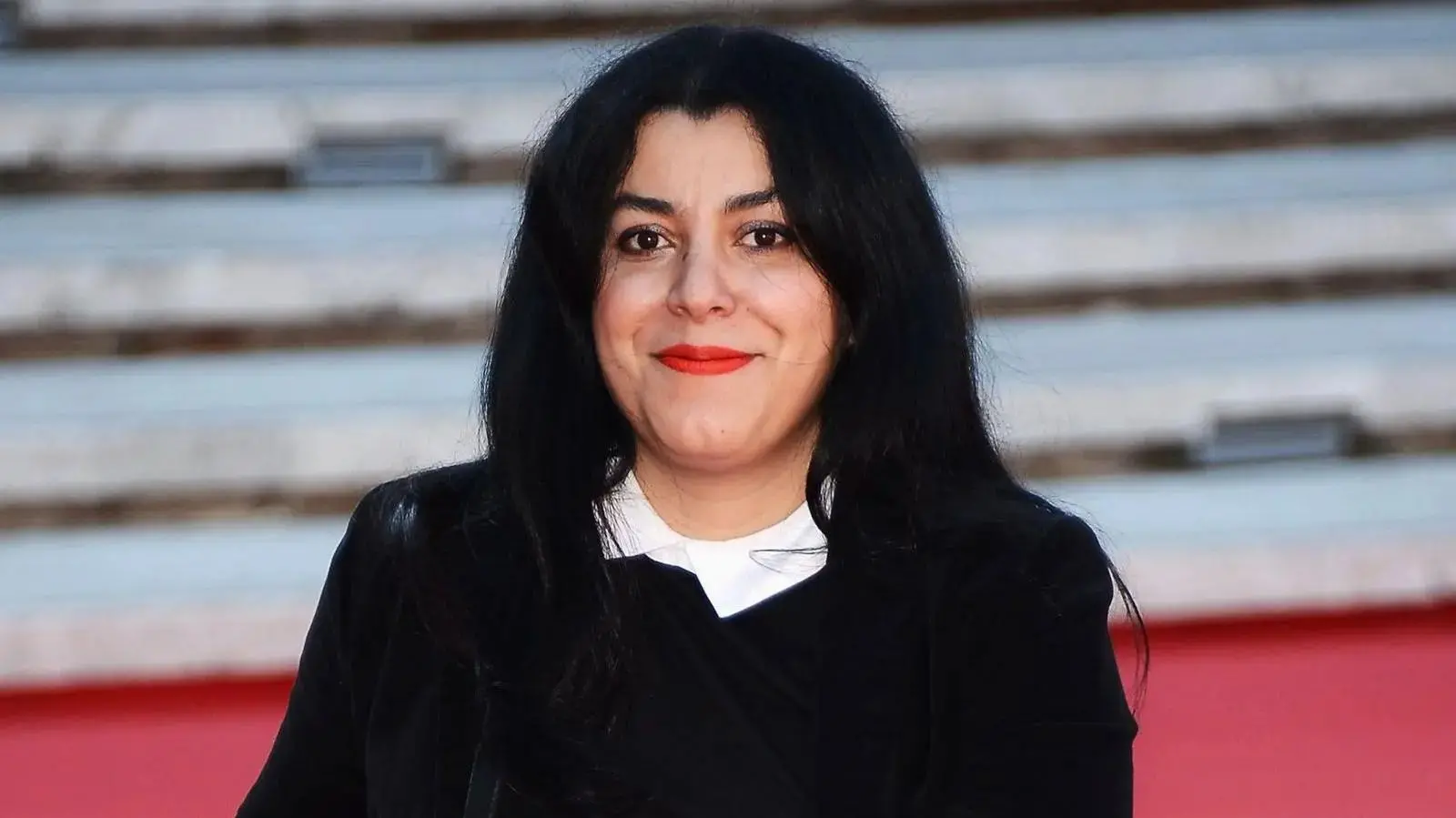 Marjane Satrapi sorri para a câmera durante evento público.