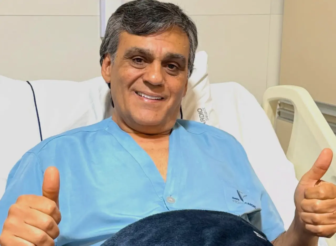 Homem branco de cabelos semi grisalhos usando bata azul de hospital.