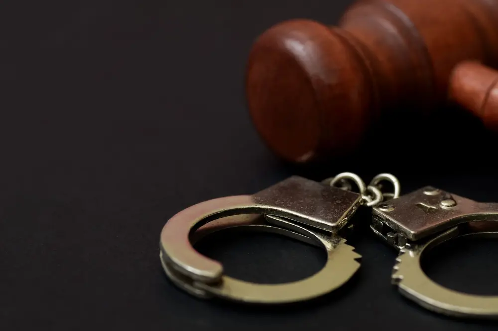 Algemas de metal e martelo de madeira do juiz no fundo preto simbolizando a aplicação da lei, o sistema de justiça criminal e a punição legal.