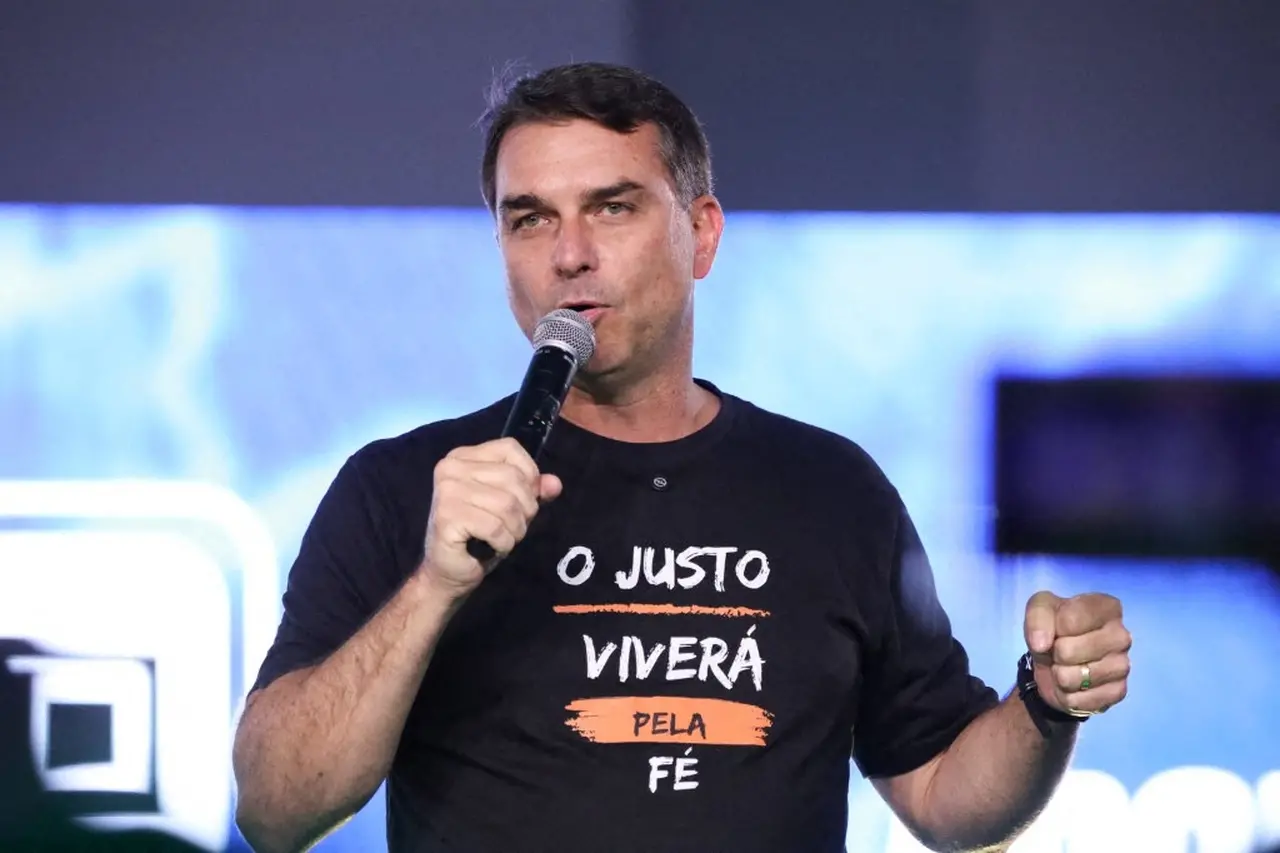 Flávio Bolsonaro, homem branco com blusa preta, discursando com microfone.