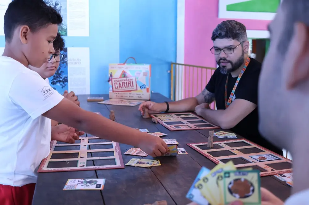 Crianças e adultos jogam cartas coloridas em volta de uma mesa.