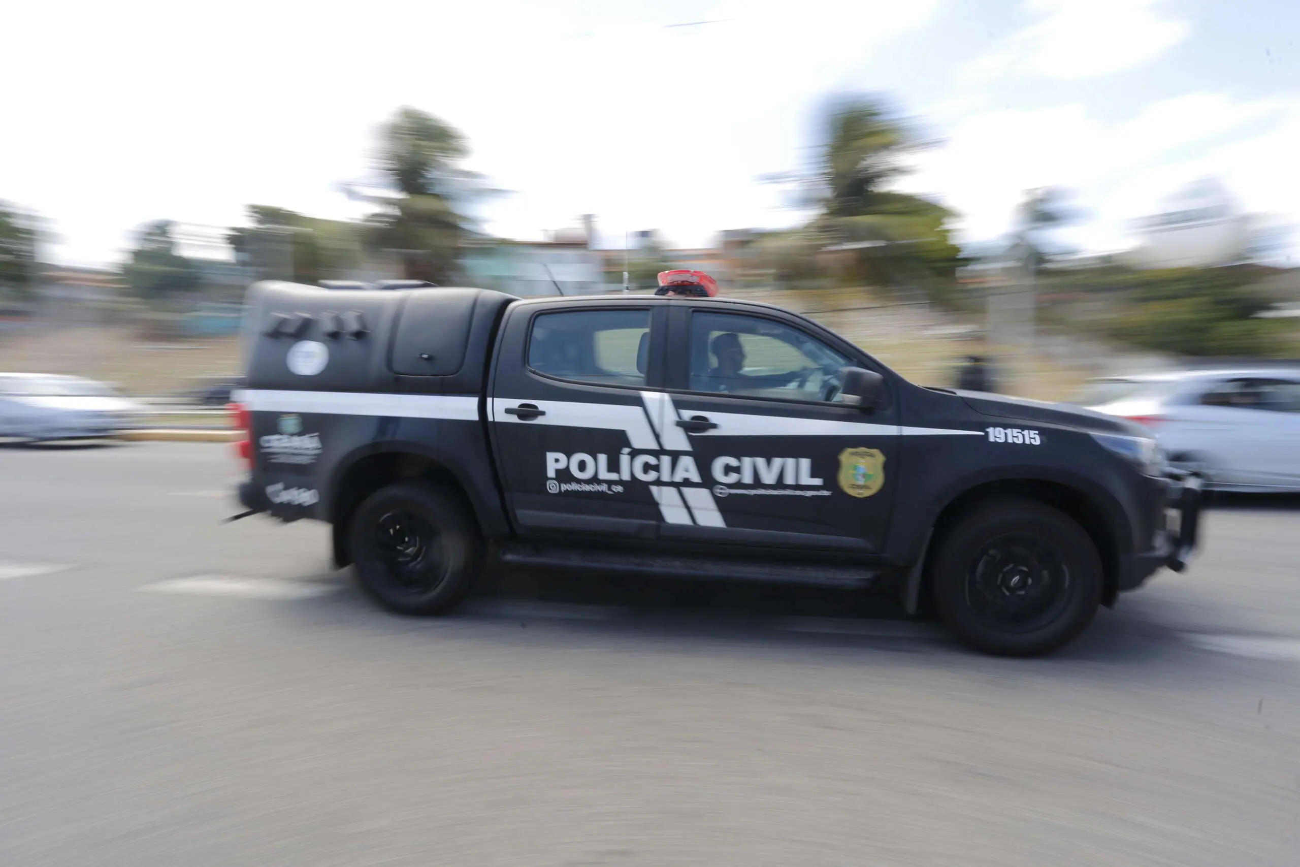 Viatura da Polícia Civil do Ceará em movimento por uma via urbana durante o dia, com efeito de desfoque no fundo que transmite sensação de velocidade. O veículo preto exibe a identificação 
