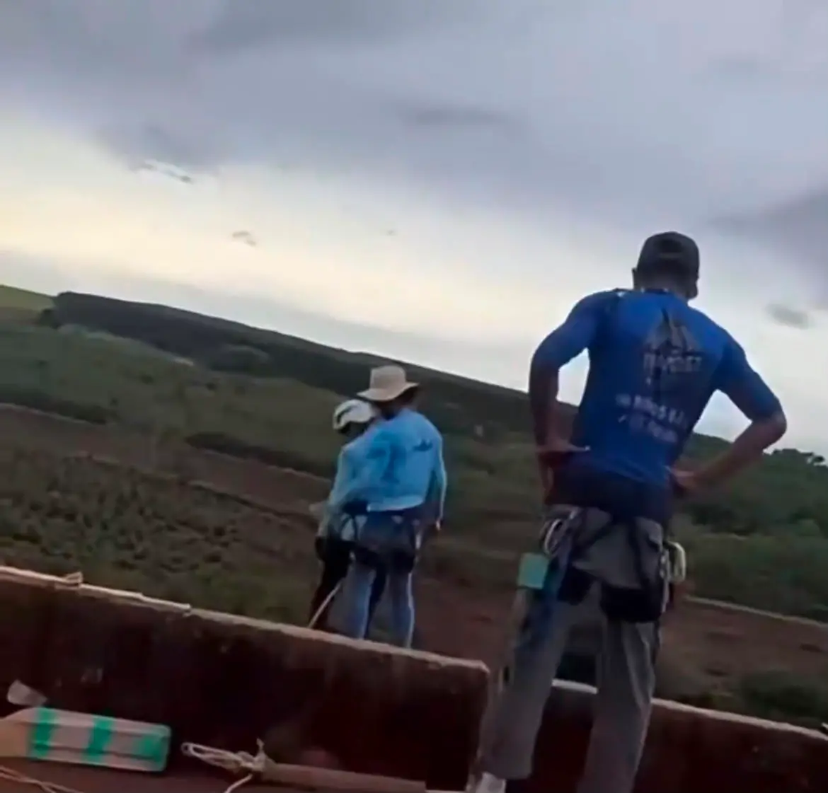 Print de vídeo em que três homens de uniforme azul e chapéu na cabeça ficam parados na plataforma de uma ponte após terem atirado mulher.
