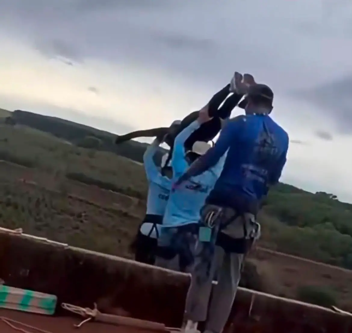 Print de vídeo em que homens de roupas azuis erguem jovem mulher com capacete na beira da plataforma de uma ponte em São Paulo.