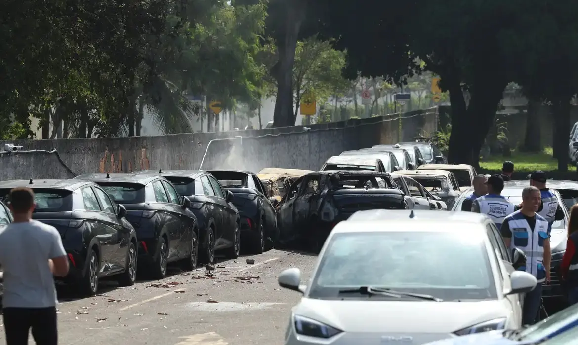 Foto que contém carros estacionados em um pátio. Destroços de helicópteros também são observados.