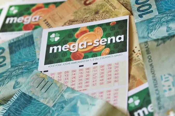 Bilhete da Mega-Sena em primeiro plano, com sua grade de números impressa em rosa, sobre uma superfície coberta por várias cdulas de dinheiro brasileiro, incluindo notas de 100 reais. O bilhete exibe o logotipo verde da Mega-Sena e ilustrações de moedas douradas ao fundo.