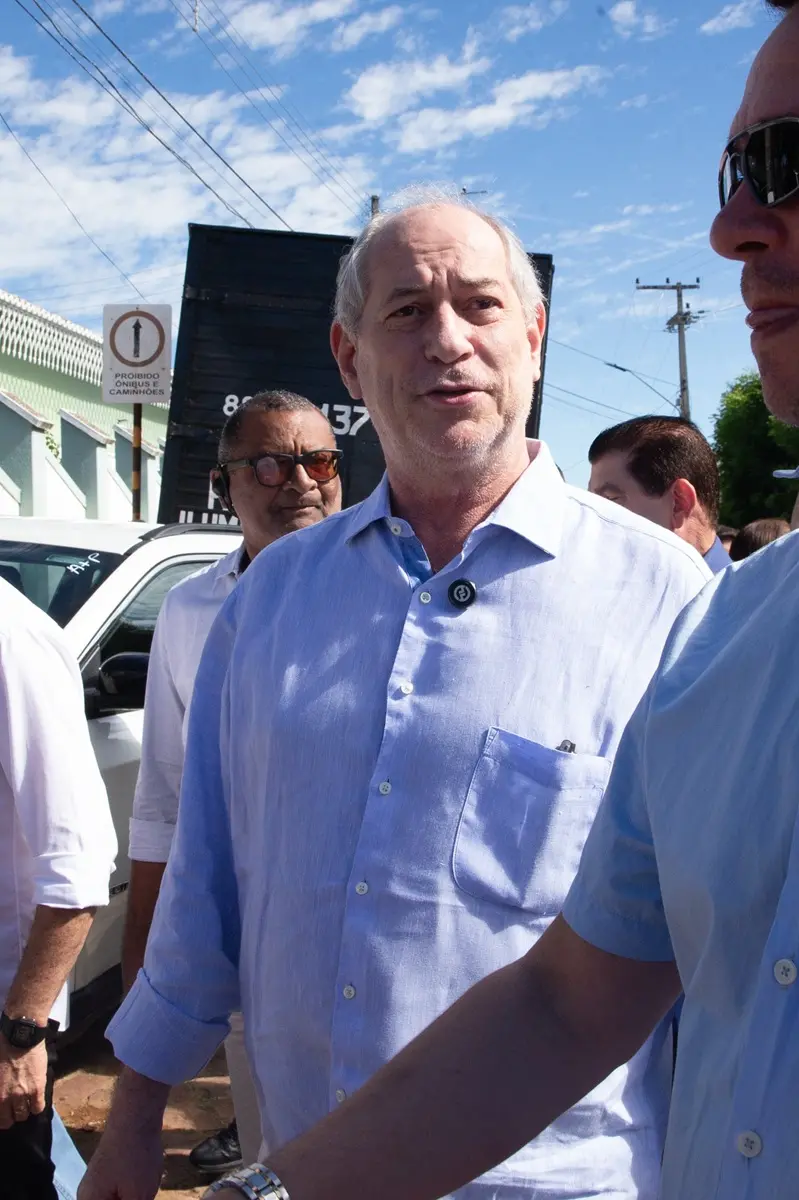 Ciro Gomes de camisa social azul-clara caminha por uma rua durante atividade pública ao ar livre, cercado por outras pessoas.