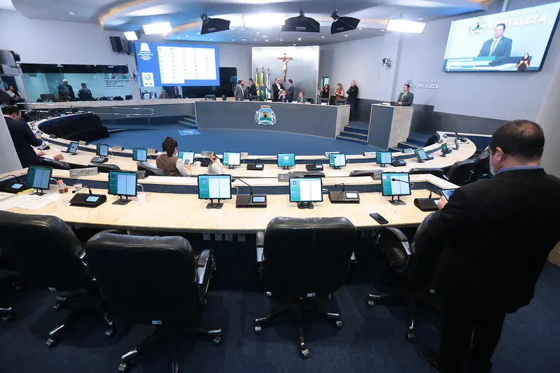 Mesa redonda de um Plenário, com diversas cadeiras vagas e alguns poucos parlamentares sentados.