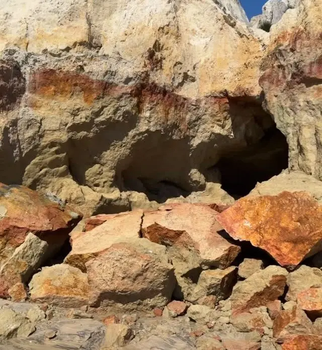 Pedra e rochas expostas com diferentes tons de amarelo, laranja e marrom, formando cavidades e buracos na encosta rochosa, com textura áspera e sedimentar ao sol.