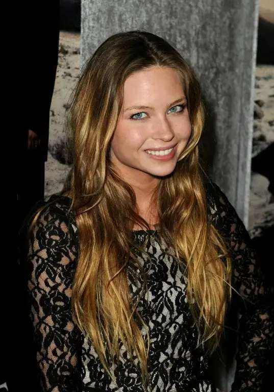 Daveigh Chase sorridente com cabelo longo castanho-claro e vestido de renda escura com fundo desfocado de cortina ao lado que fez O Chamado morre aos 35 anos.