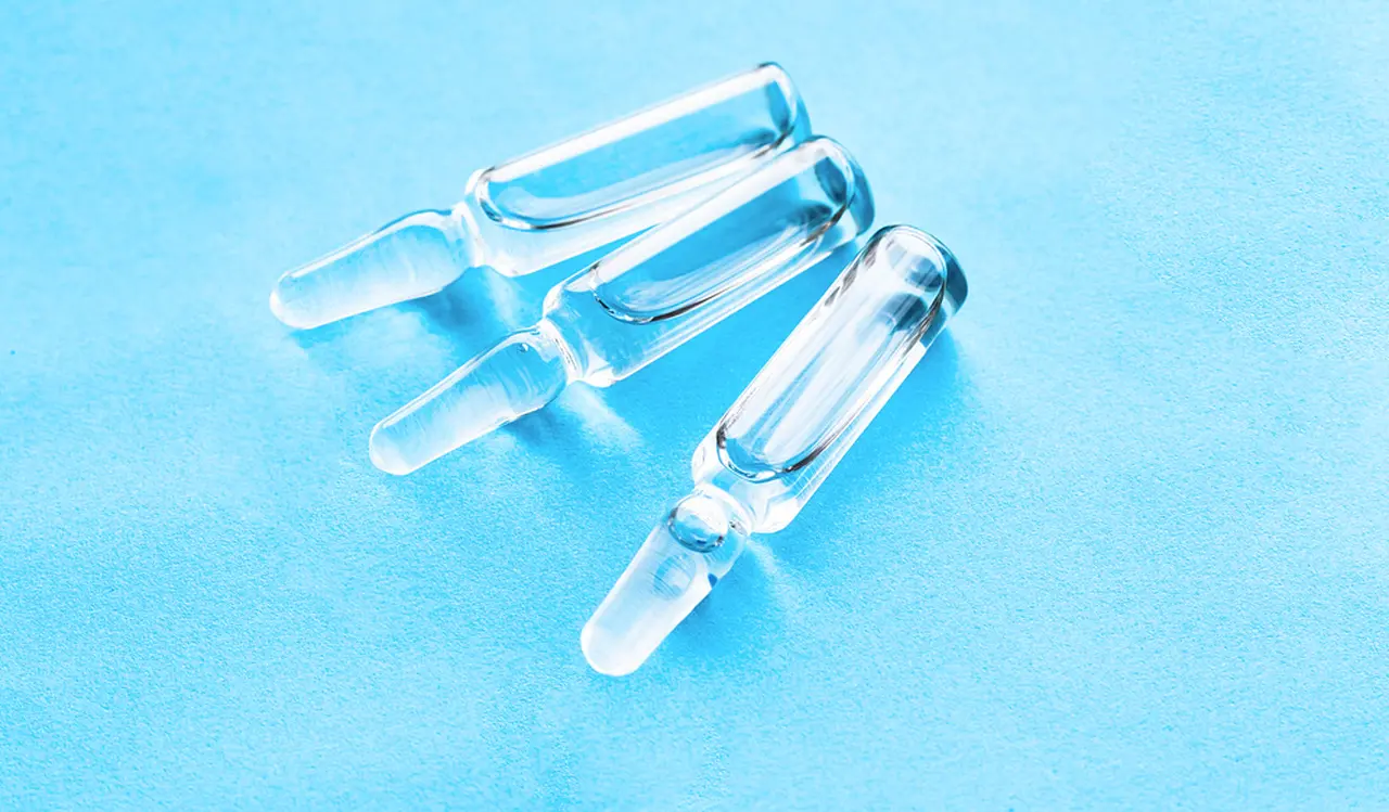 Ampolas de vidro transparentes com líquido incolor, dispostas sobre superfície azul clara.