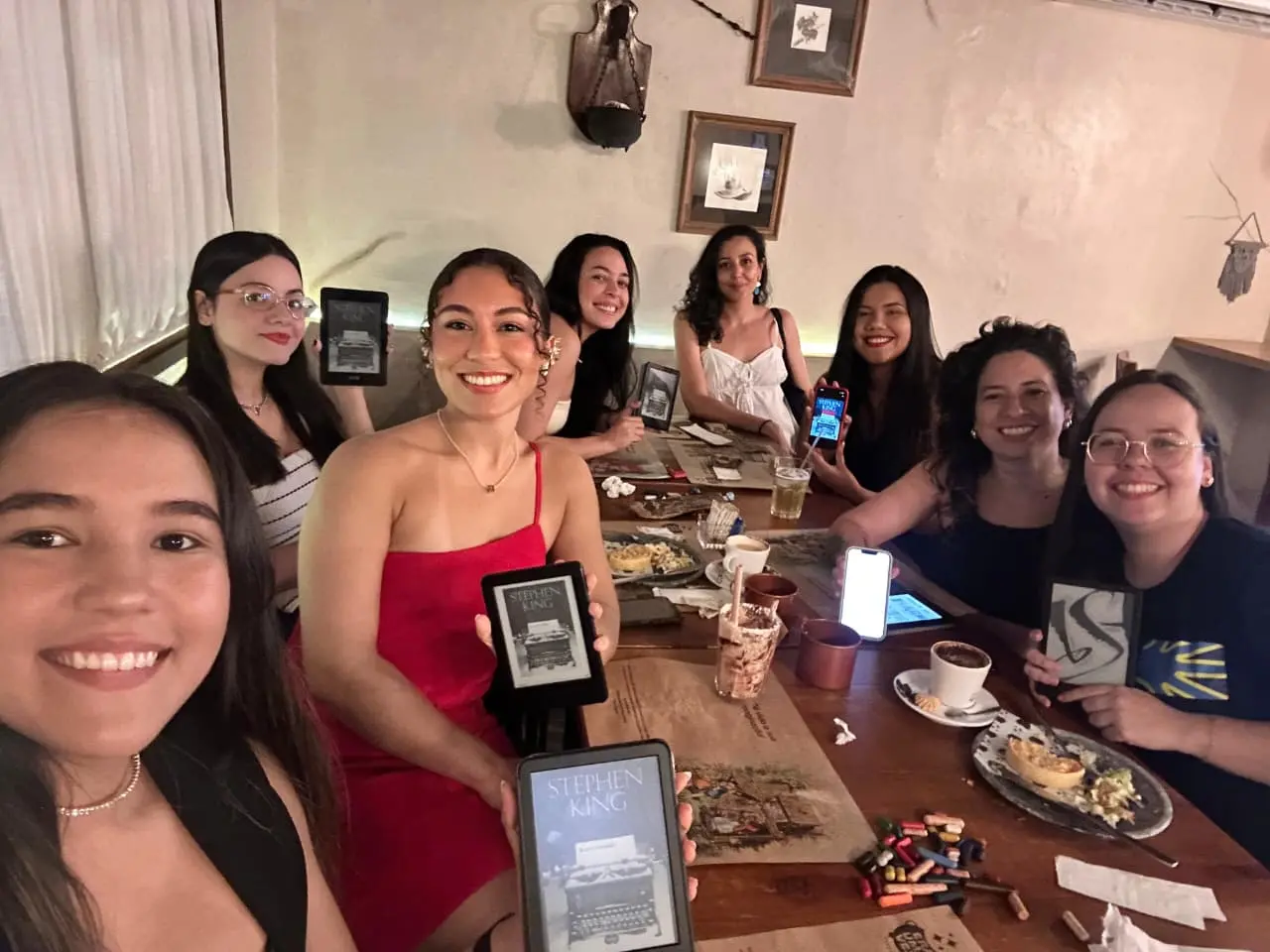 Grupo de mulheres participa de um encontro de clube de leitura dentro de um café sentadas à mesa. 
