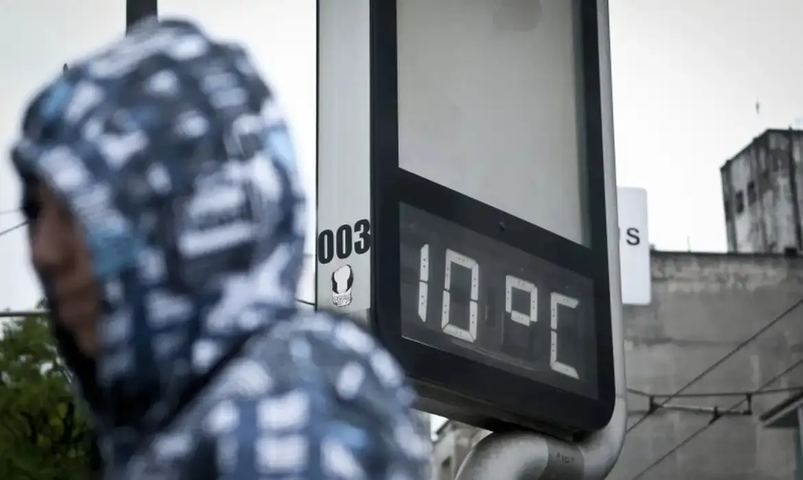 Homem anda agasalhado enquanto painel mostra temperatura de 10 graus.