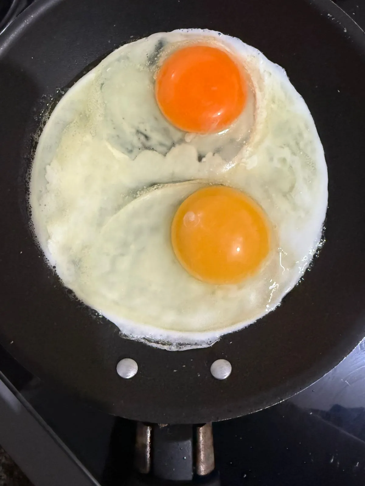 Dois ovos em uma frigideira, um de galinha caipira, com a gema muito mais laranja vibrante e um de granja, com a gema mais amarela.
