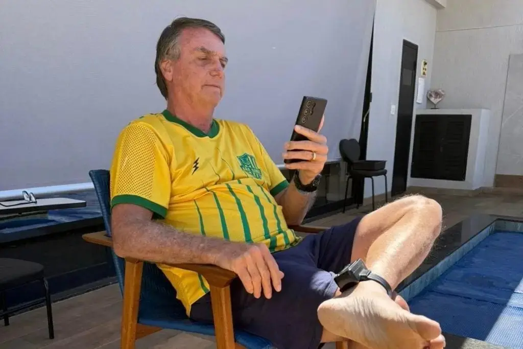 foto de Bolsonaro sentado em cadeira na varanda de casa mostrando tornozeleira eletrônica.