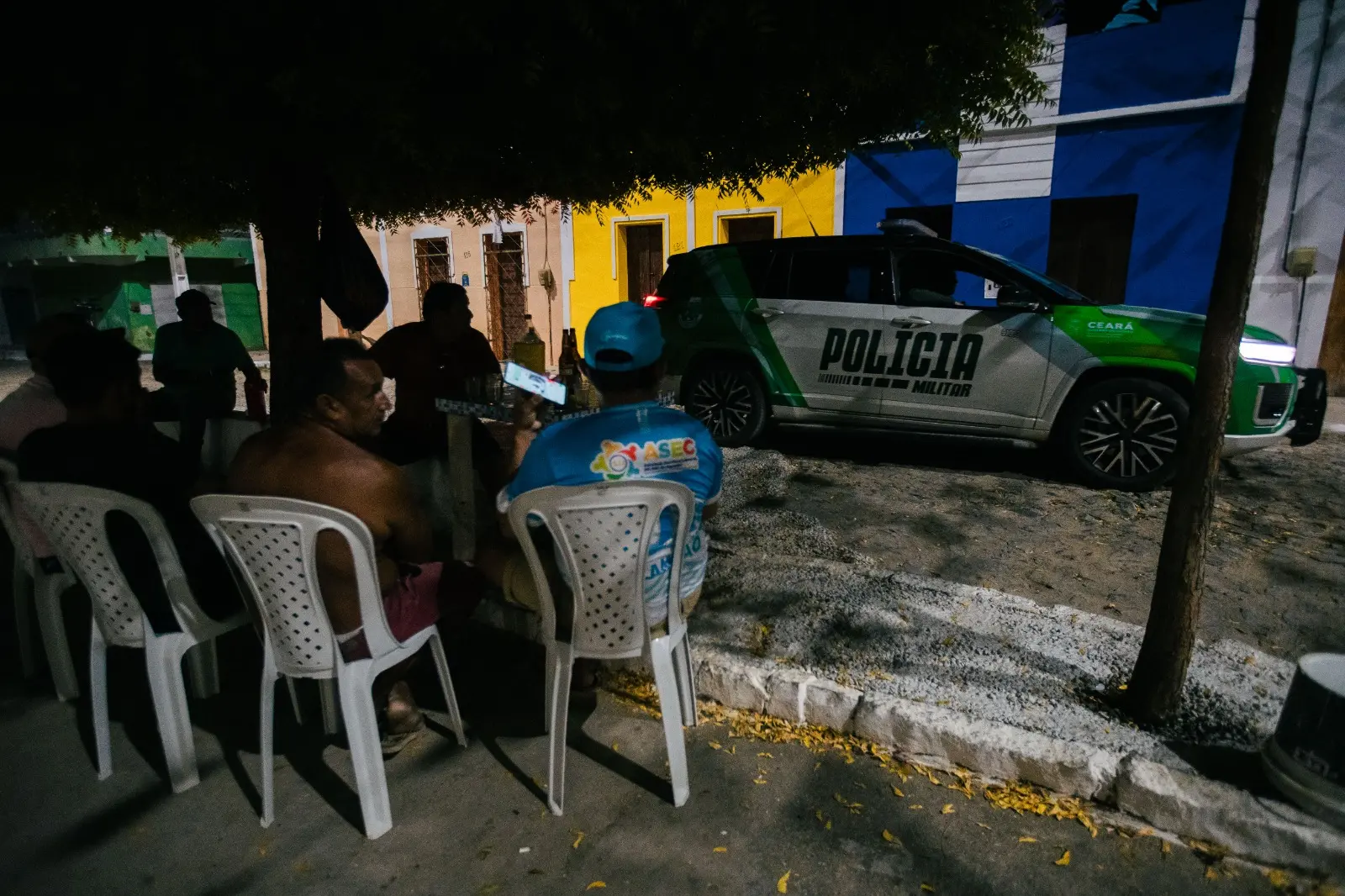 Pessoas conversando na rua e, ao fundo uma viatura da Polícia 