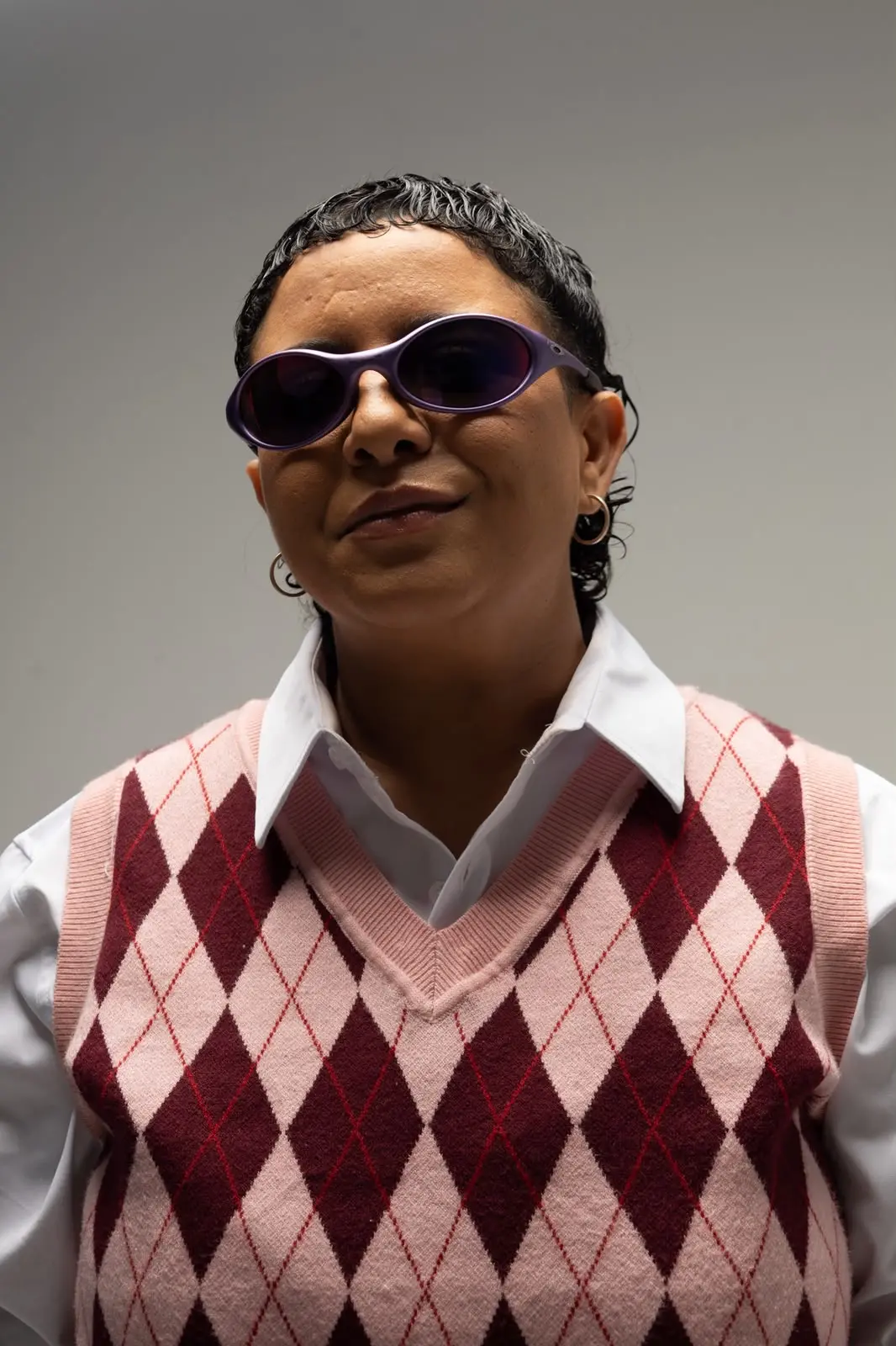 Mulher de cabelo curto, óculos de sol e camisa com estampa rosa e vermelha olhando para a câmera.