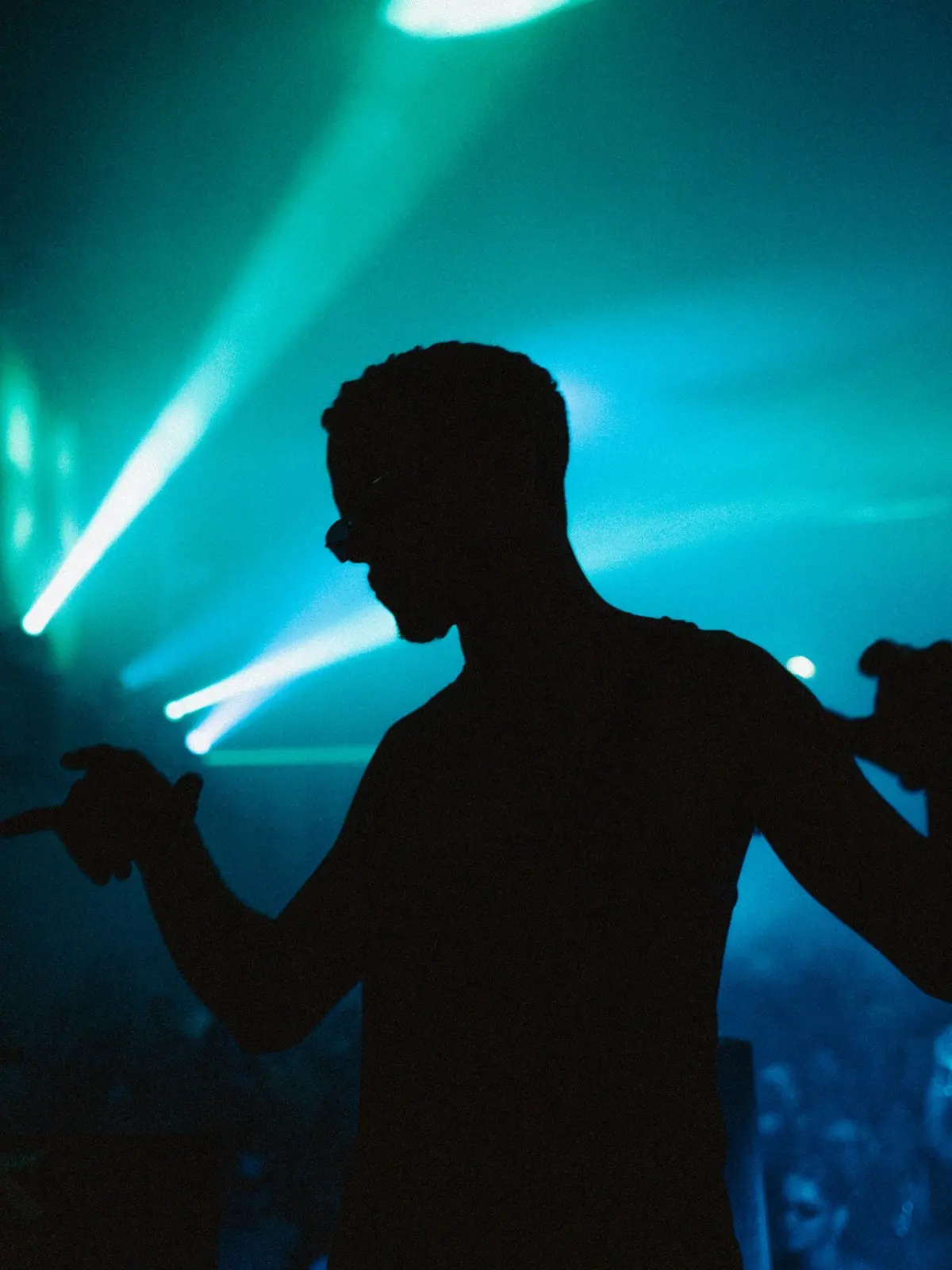 Foto da silhueta de um homem em posição de dança. Atrás dele, freixos de luzes azuis iluminam o local.