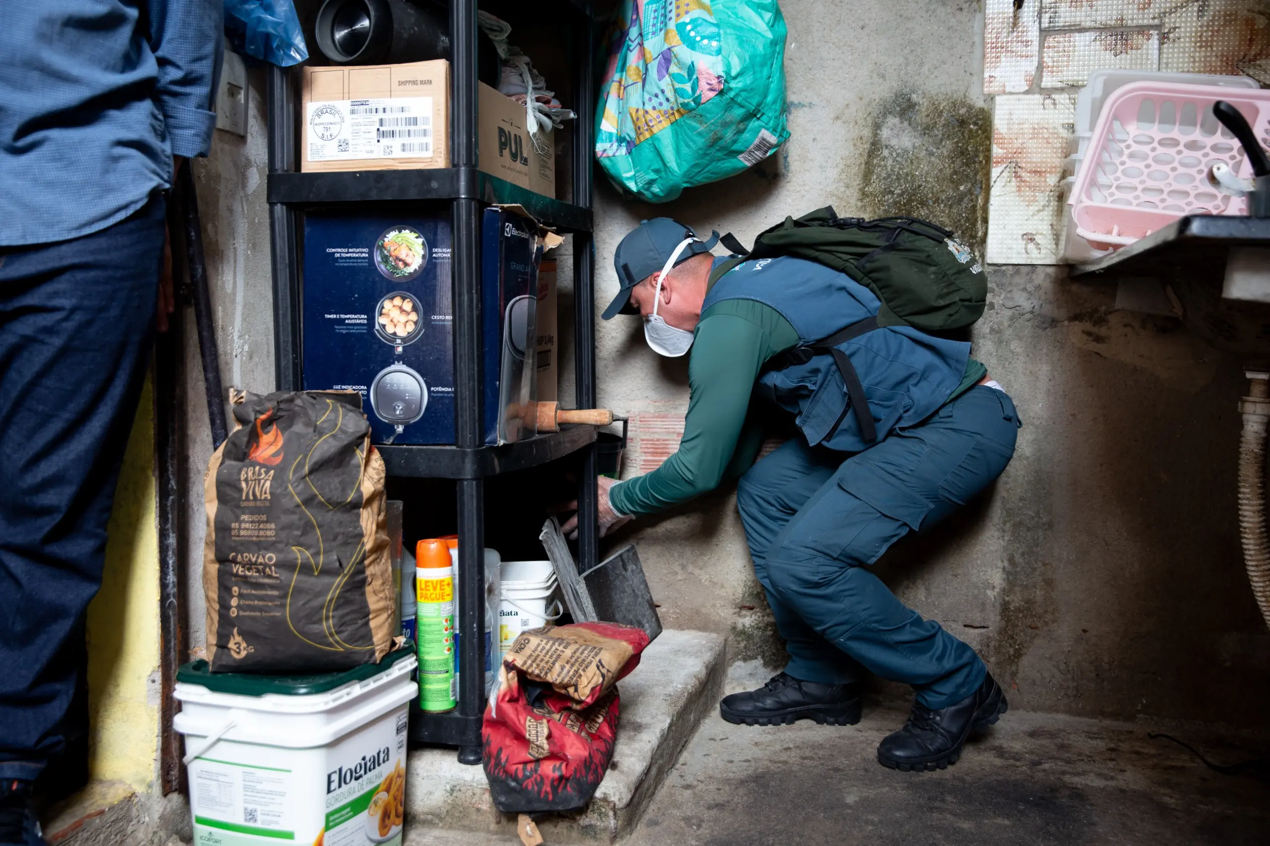 Agente de Endemias uniformizado, com máscara e luvas, instalando Armadilhas de Mosquitos, as Estação Disseminadora de Larvicida, em ambientes internos de uma residência para combater o Aedes aegypti