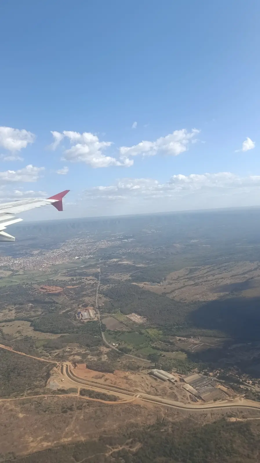 Fotografia aérea tirada da janela de um avião (com a ponta da asa visível à esquerda) mostrando a vasta extensão da Chapada do Araripe. Destacam-se áreas urbanizadas, estradas, terrenos agrícolas e trechos de vegetação nativa sob céu claro com poucas nuvens.