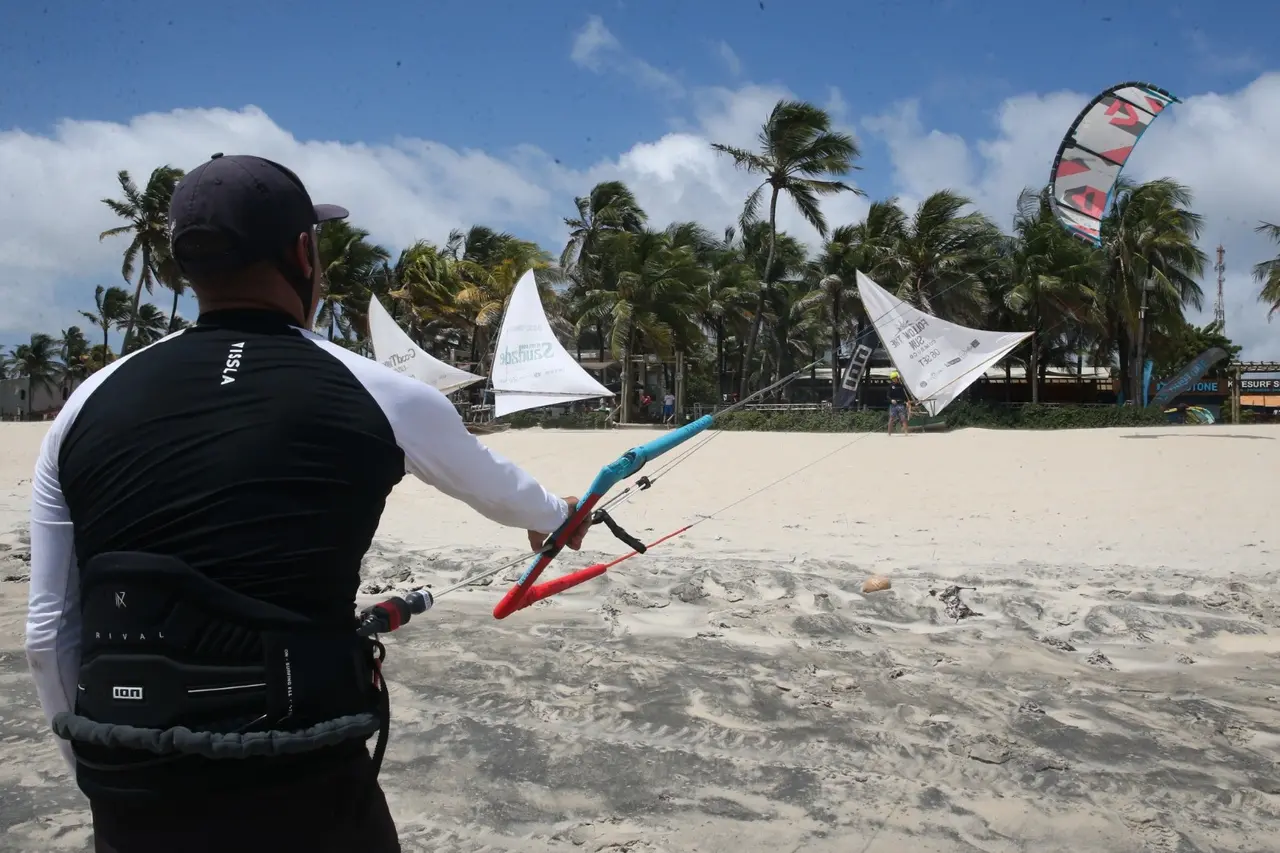 Instrutor ensinando direção do vento e como segurar pipa de kitesurf na areia.