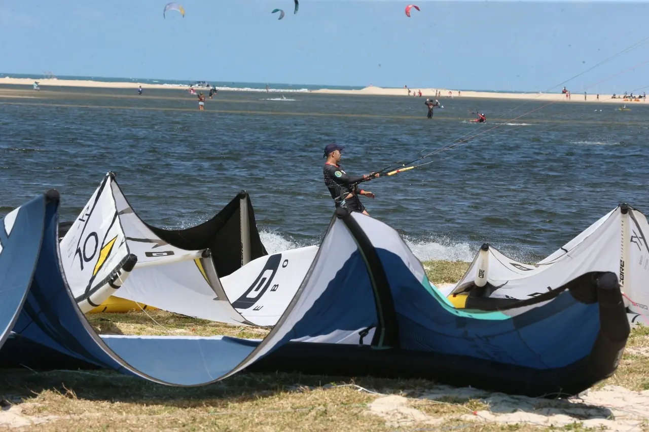 Pipa de kitesurf em primeiro plano e praticantes na água ao fundo.