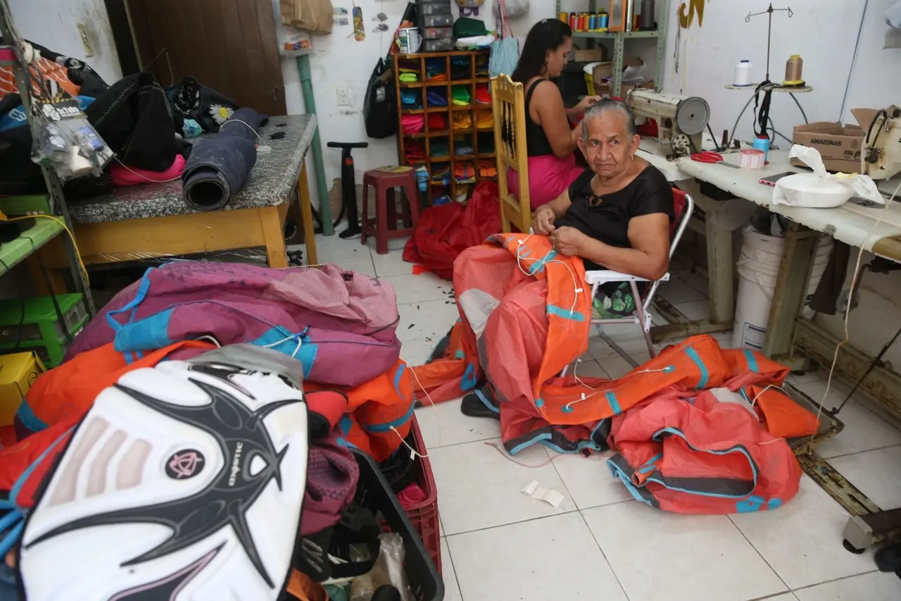 Duas mulheres fazendo serviço de costura em sala com muitas peças e partes de equipamentos de kitesurf.