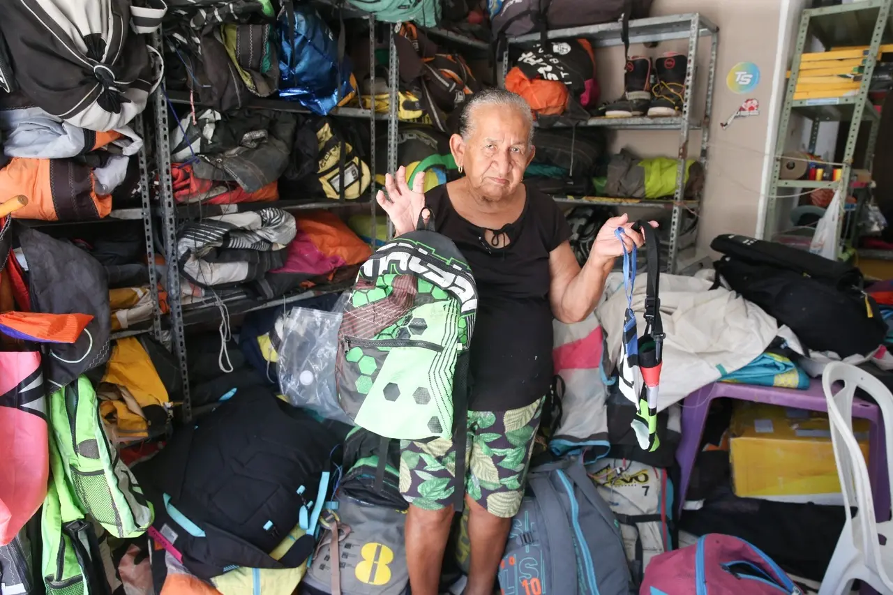 Mulher idosa segurando uma mochila verda feita de material reciclado de vela de kitesurf.