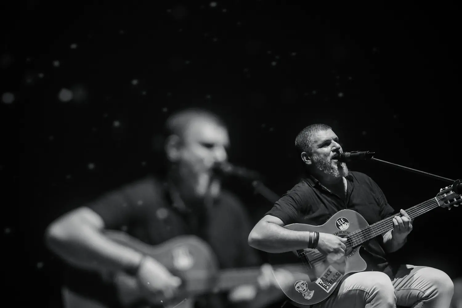Foto em preto e branco mostra o cantor tocando violão e cantando.