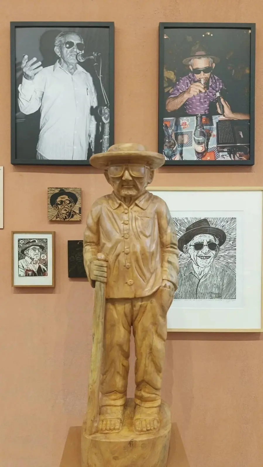Parede de exposição com fotografias coloridas, preto e branco e escultura do poeta popular Patativa do Assaré.