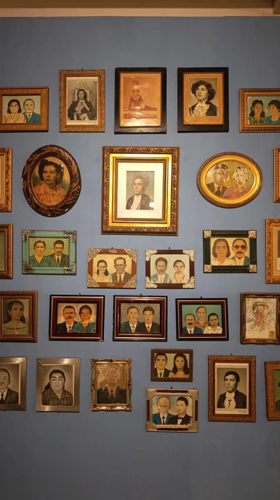 Parede de exposição azul com dezenas de retratos antigos pintados de pessoas no interior do Ceará.