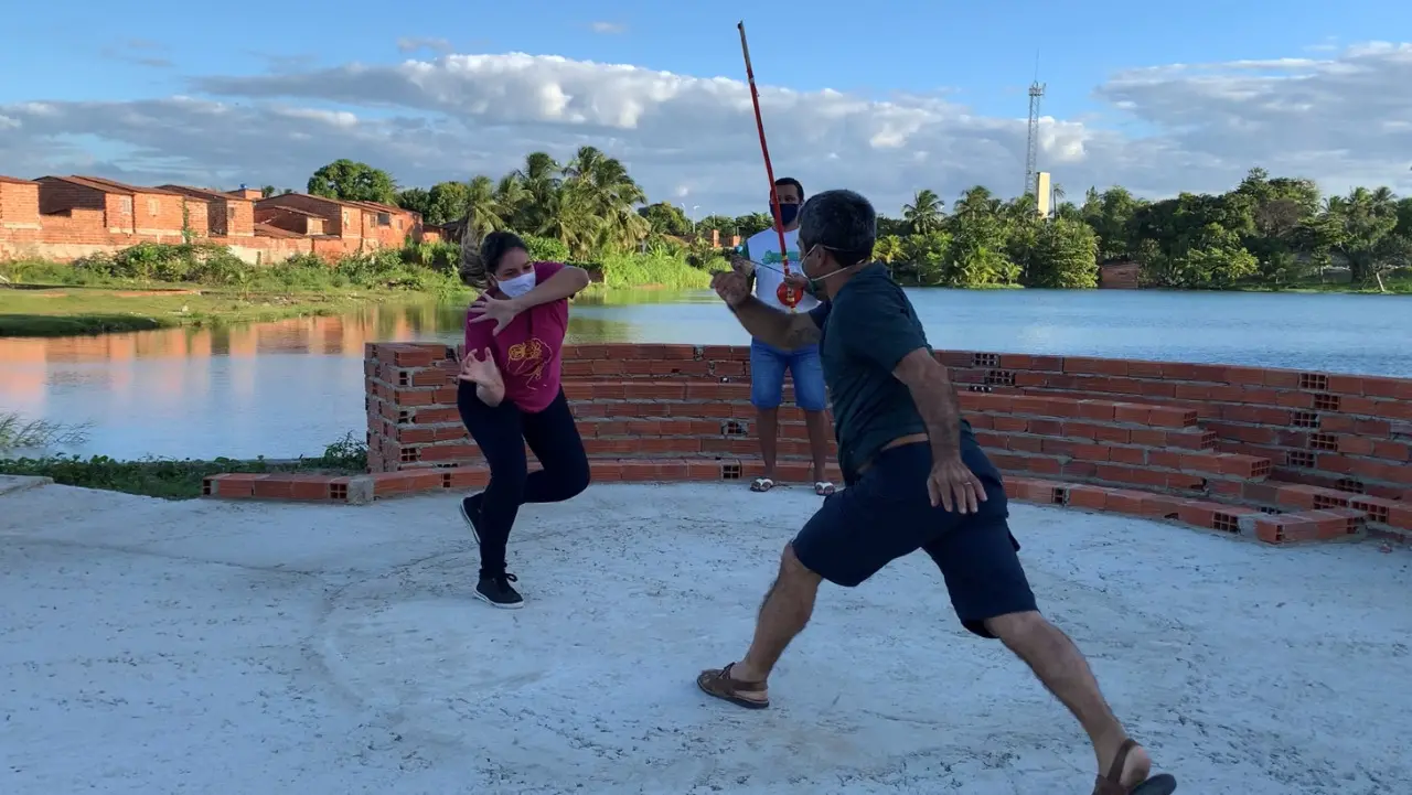 Mulher jogando capoeira com homem, lago ao fundo