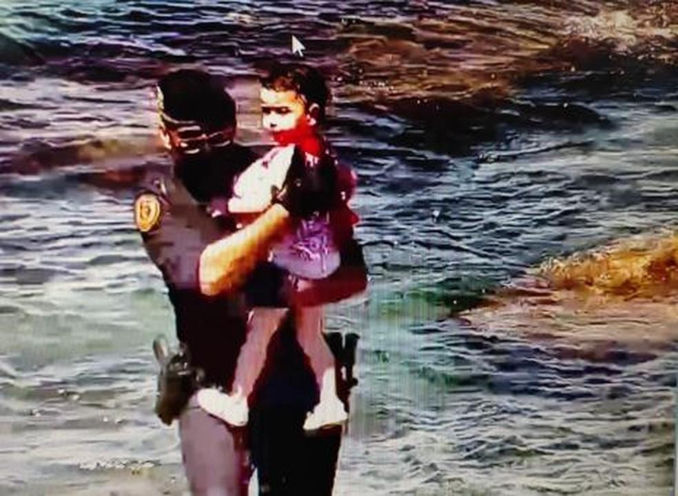 Menina de vestido sendo resgatada por policial