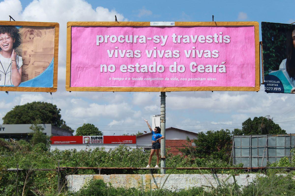 Sy Gomes posando com outdoor sobre memória travesti montado em Fortaleza