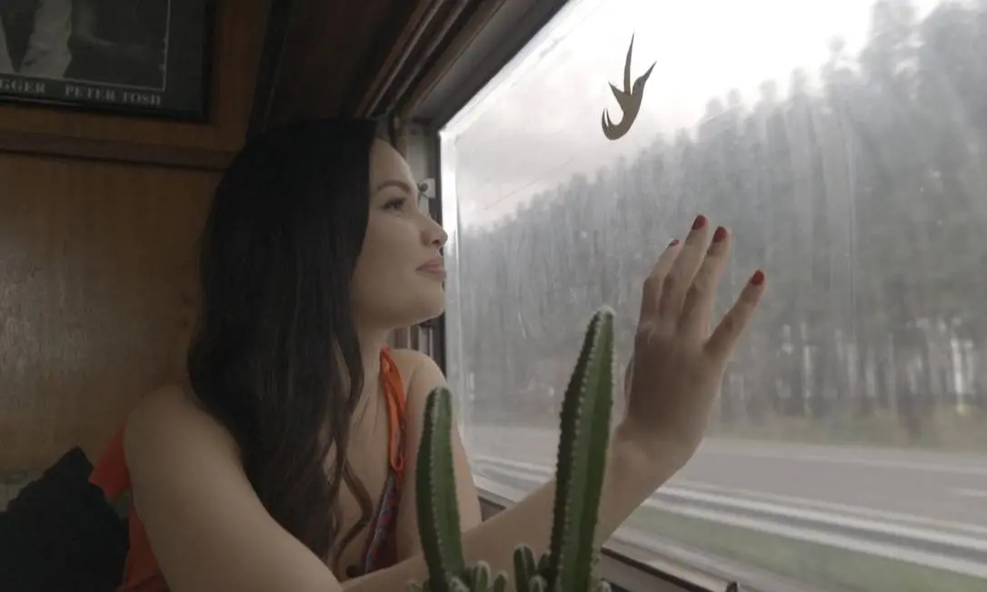 Juliette em ônibus de vestido laranja ao lado de um cacto