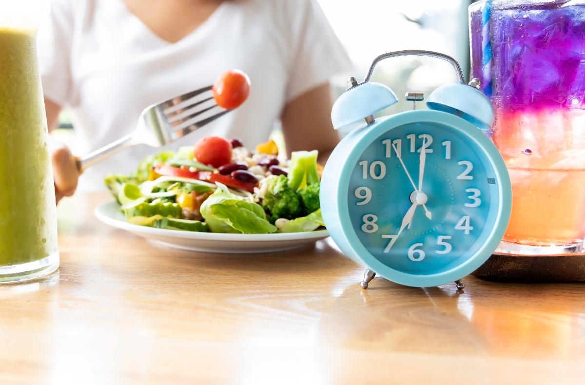 Imagem de mulher comendo salada com relógio azul do lado