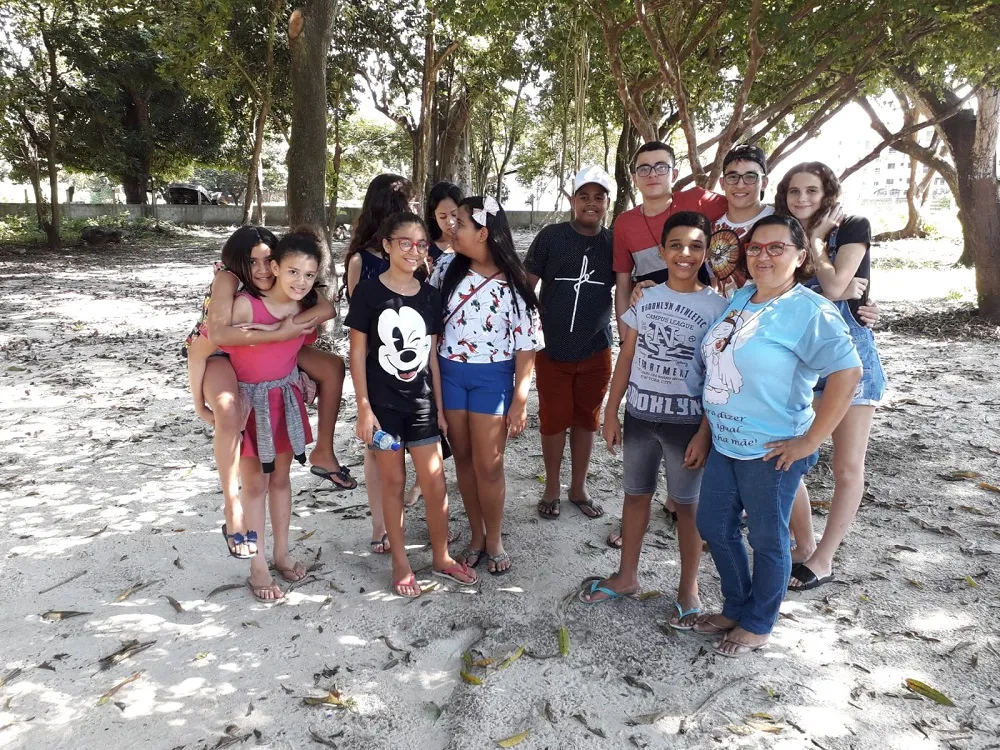 Crianças e jovens do Parque Santana reunidos à sombra do baobá, no Minimuseu Firmeza, com a mobilizadora social Silvânia Vieira