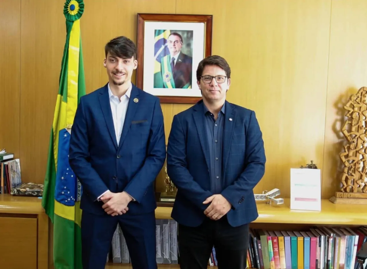 Jair Renan e Mario Frias posam em frente a retrato de Bolsonaro