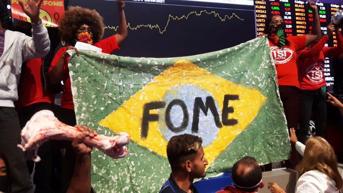Manifestantes do MTST segurando cartaz com a palavra fome escrita sobre a cartaz da bandeira do brasil na bolsa de valores