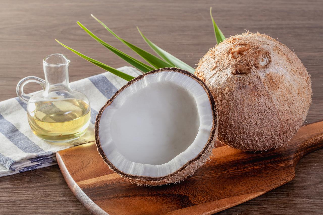Óleo de coco em uma garrafa com coco e folhas de palmeira verde em uma mesa de madeira