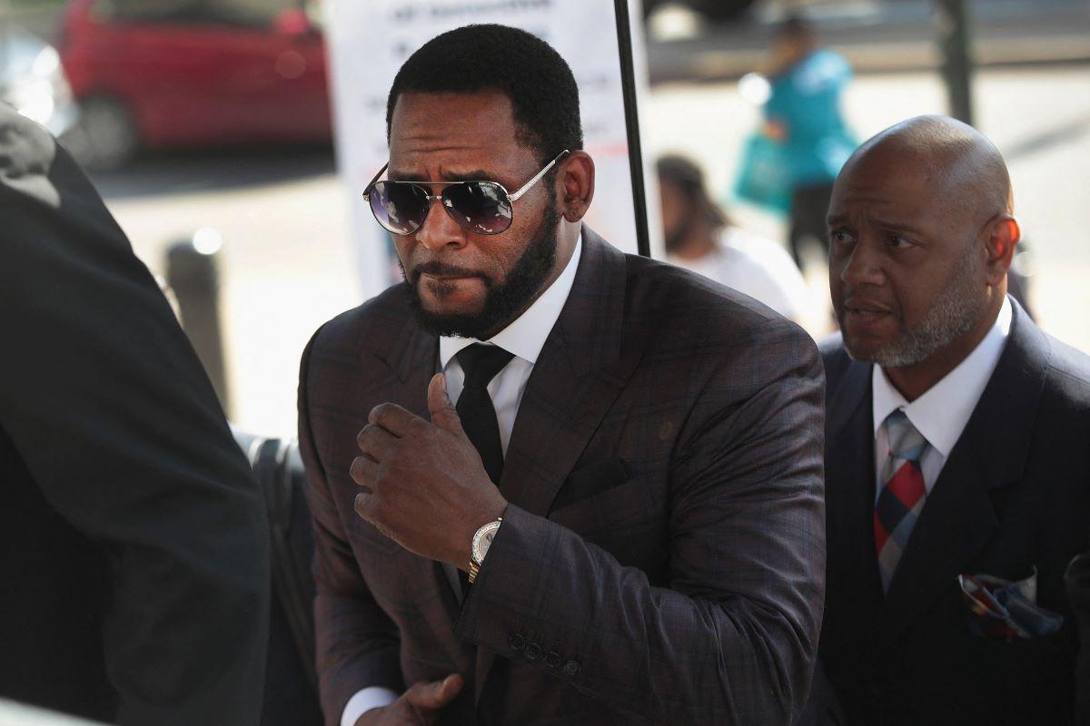 R. Kelly entrando em julgamento vestido de terno preto e óculos escurso