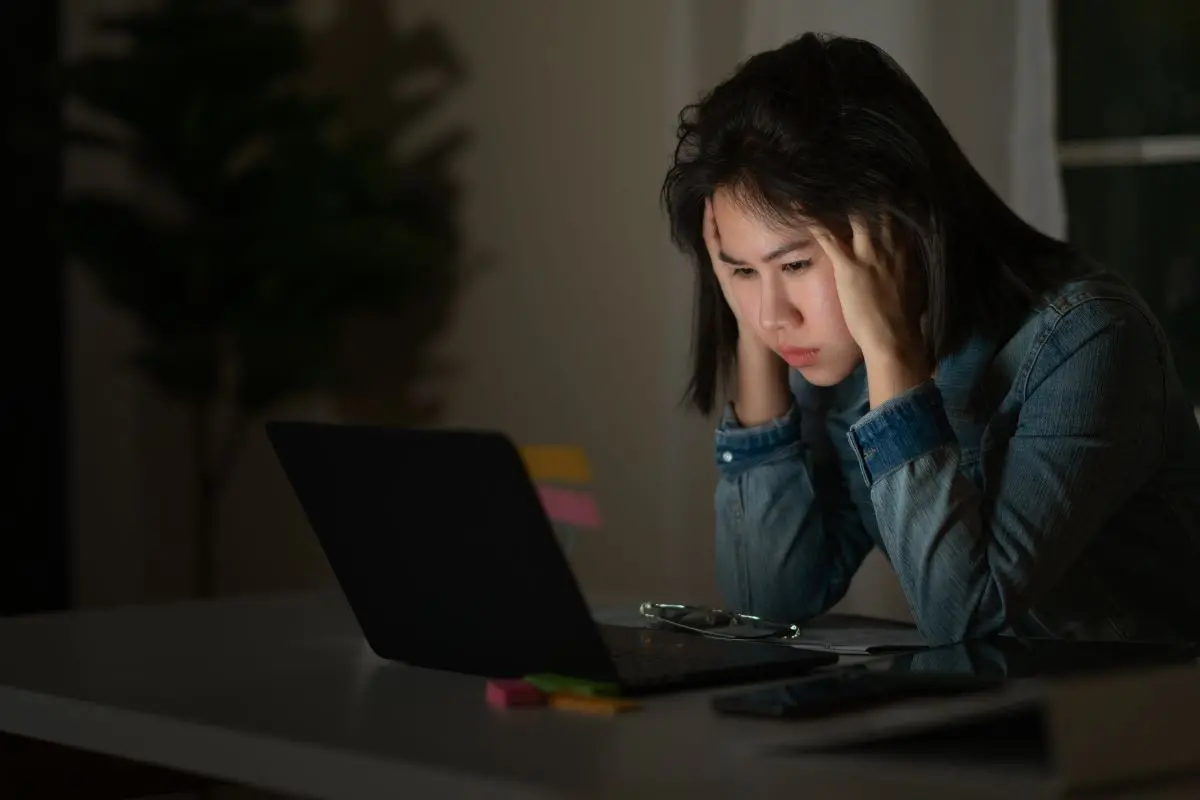 Mulher com a mão na cabeça em frente a notebook
