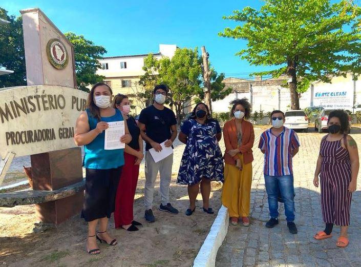 sete pessoas de máscara diante de placa com o nome do ministério público