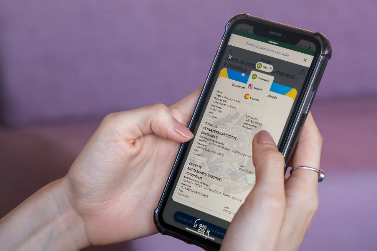 mãos seguram celular com imagem do comprovante de vacinação contra covid-19