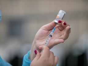 Imagem de uma mão com uma seringa e frasco com vacina de covid