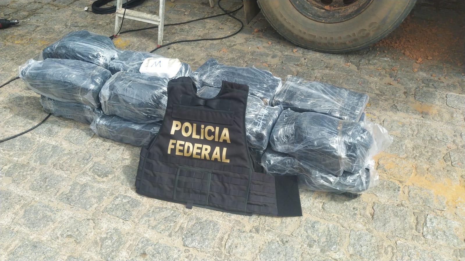 200 quilogramas de cocaína embaladas em sacos pretos dispostos sobre o chão e com um colete a prova de balas da polícia federal em cima